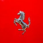 Close-up of a luxury car emblem on a glossy red surface displaying elegance and style.